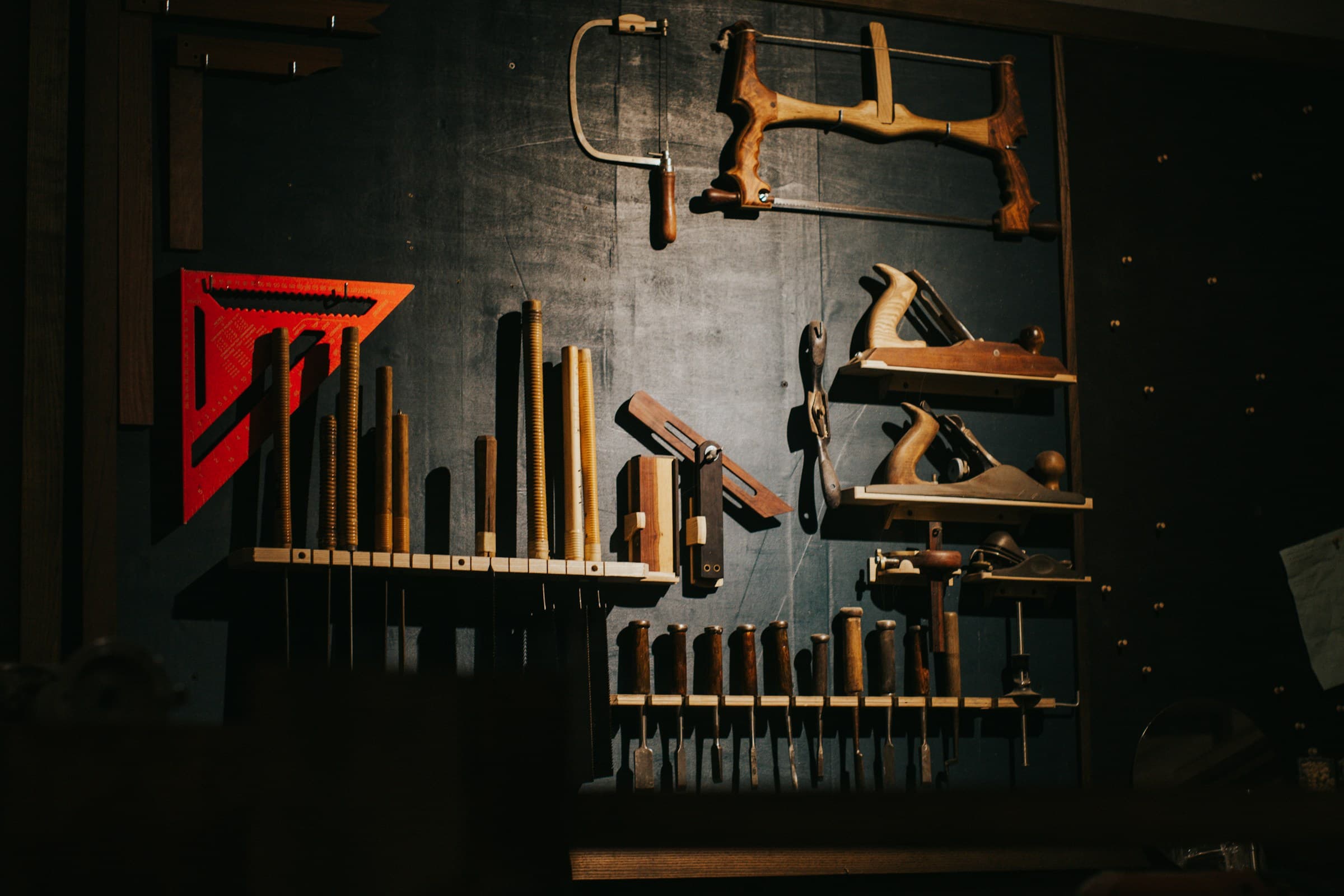 Various woodworking tools hanging in an organized grid on a dark workshop wall